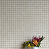 A vase of flowers stands in front of a wall papered in a dense plaid pattern in shades of gray.