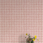 A vase of flowers stands in front of a wall papered in a dense plaid pattern in shades of cream and red.