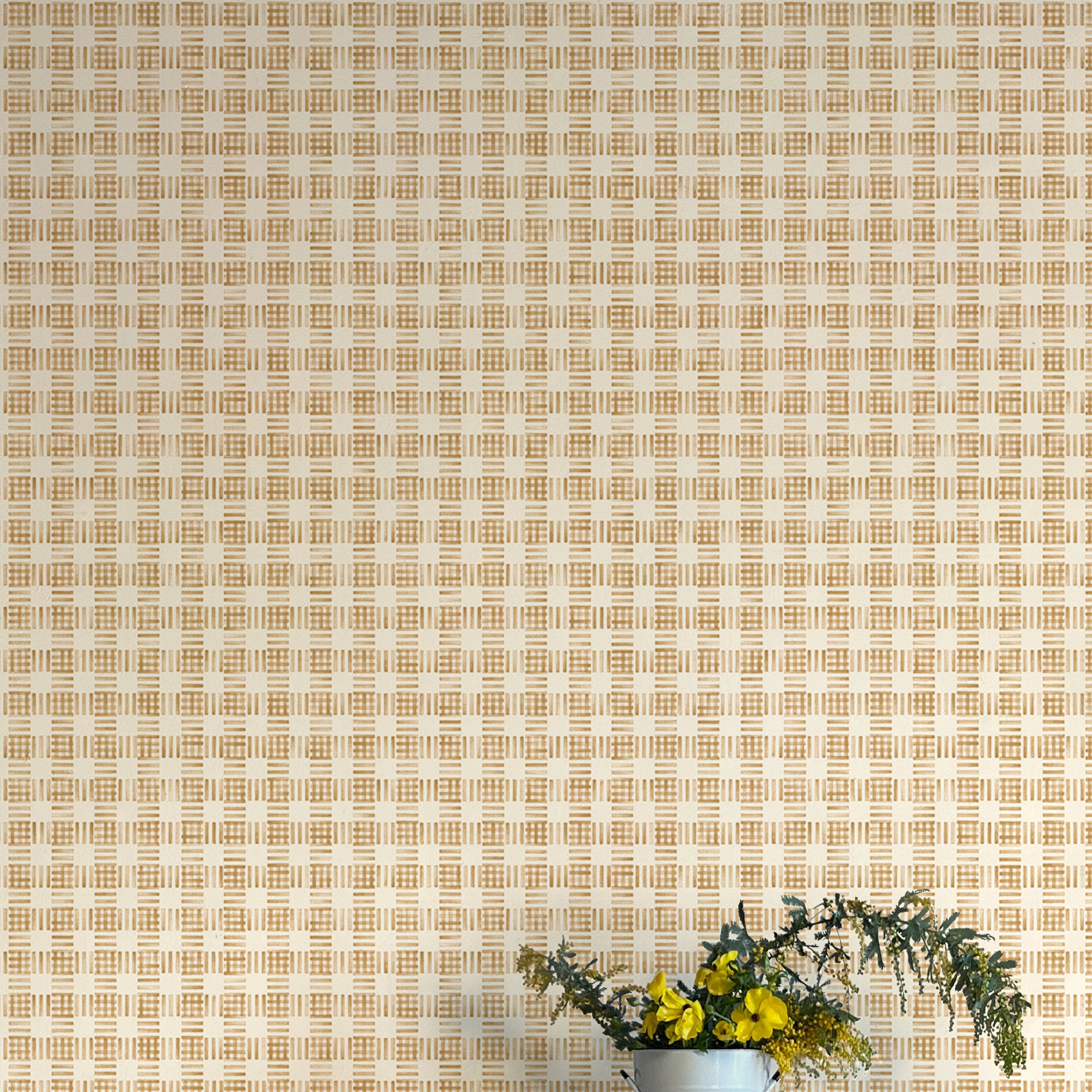 A vase of flowers stands in front of a wall papered in a dense plaid pattern in shades of orange and tan.