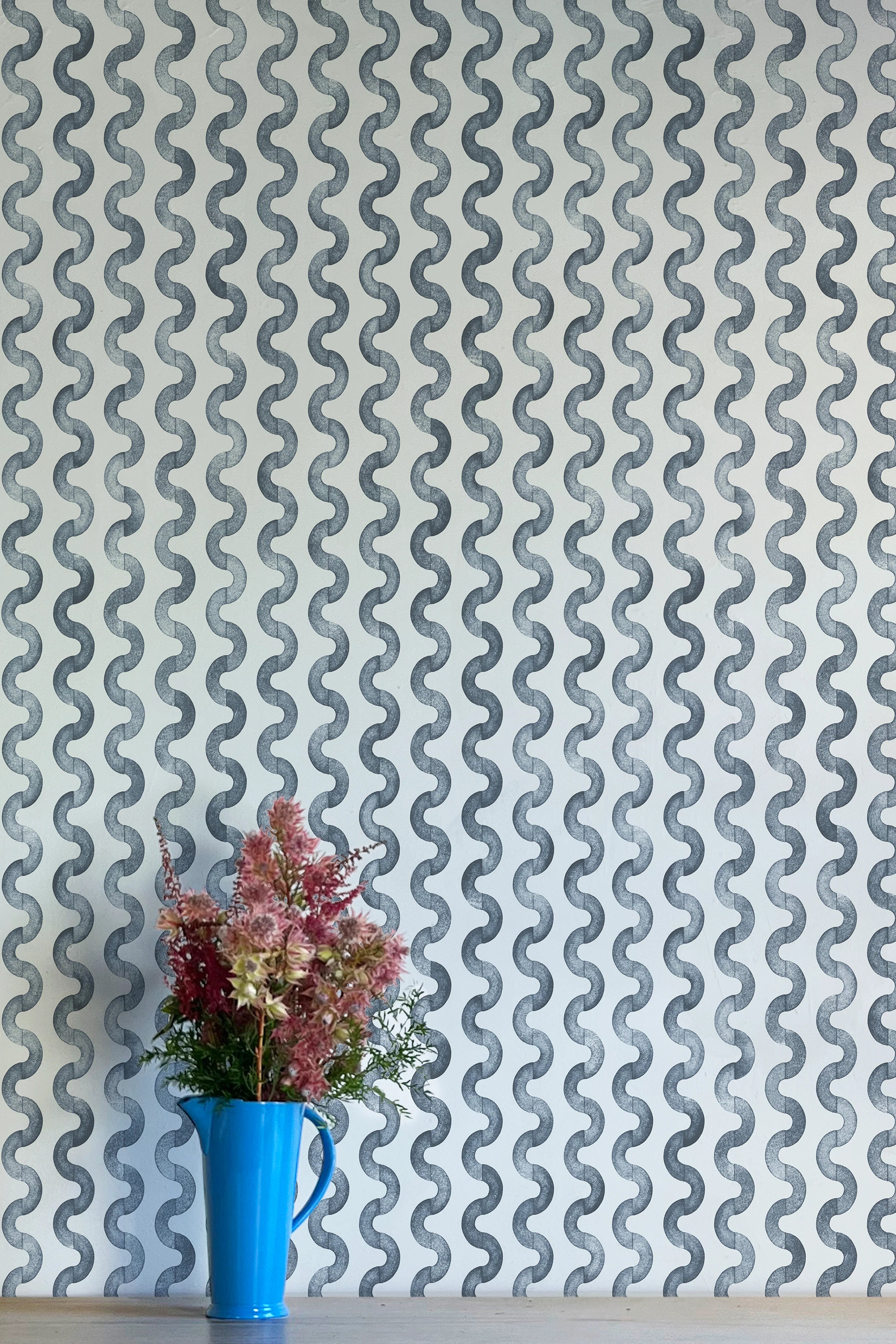 A vase of flowers stands in front of a wall papered in a playful curvy stripe print in navy on a light blue field.