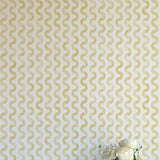 A vase of flowers stands in front of a wall papered in a playful curvy stripe print in yellow on a cream field.