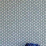 A vase of flowers stands in front of a wall covered in a minimalist quatrefoil pattern in gray on a blue field.