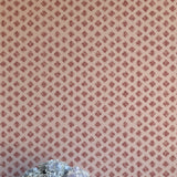 A vase of flowers stands in front of a wall covered in a minimalist quatrefoil pattern in red on a cream field.