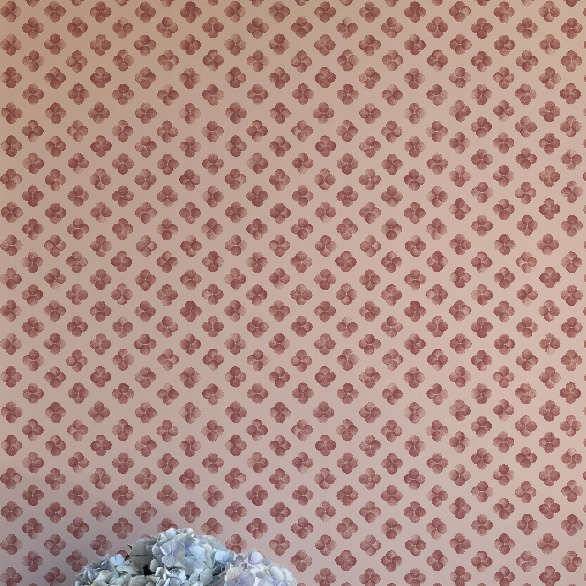 A vase of flowers stands in front of a wall covered in a minimalist quatrefoil pattern in red on a cream field.