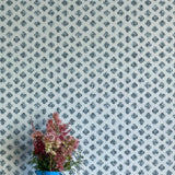 A vase of flowers stands in front of a wall covered in a minimalist quatrefoil pattern in navy on a light blue field.