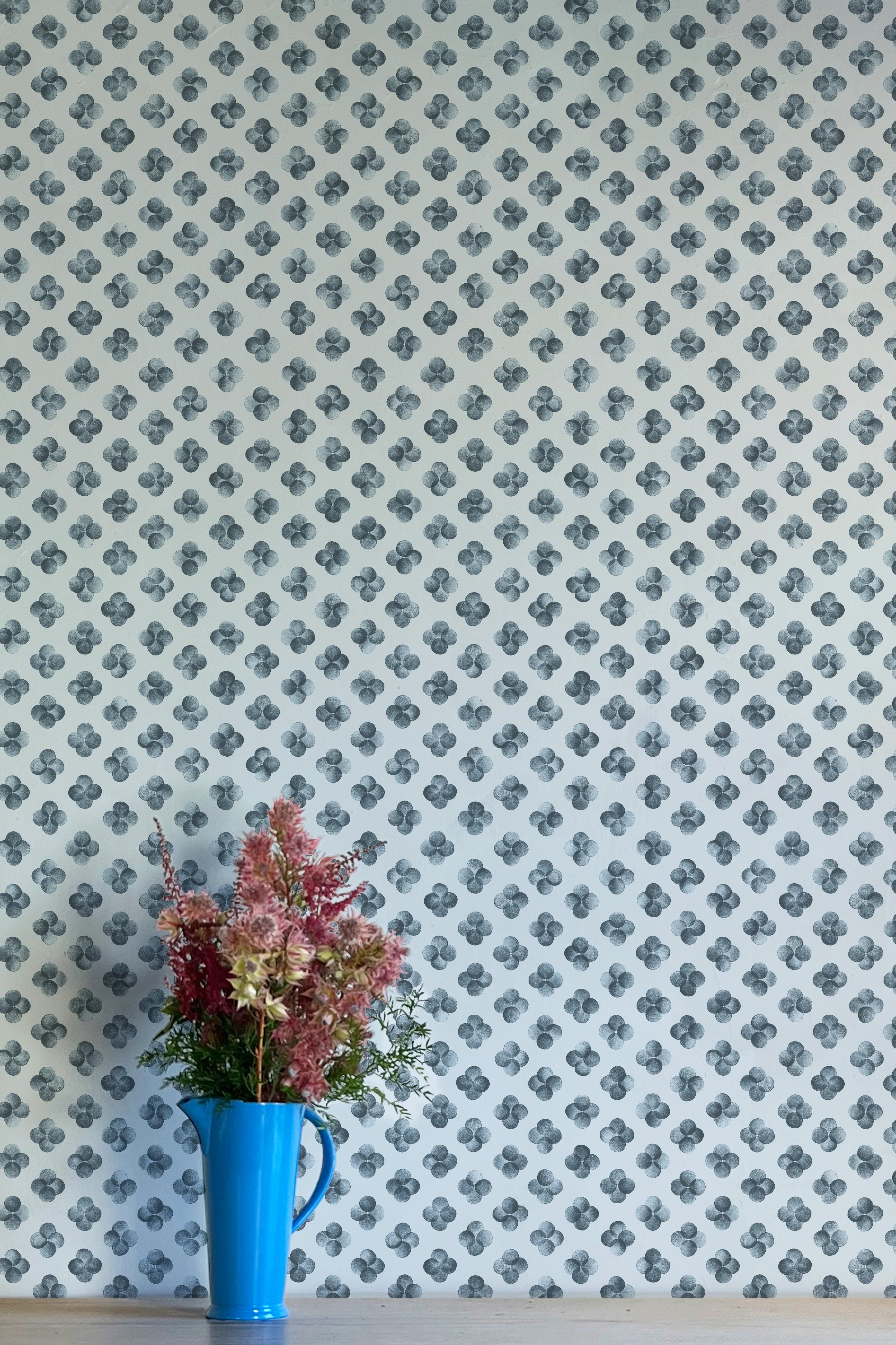 A vase of flowers stands in front of a wall covered in a minimalist quatrefoil pattern in navy on a light blue field.