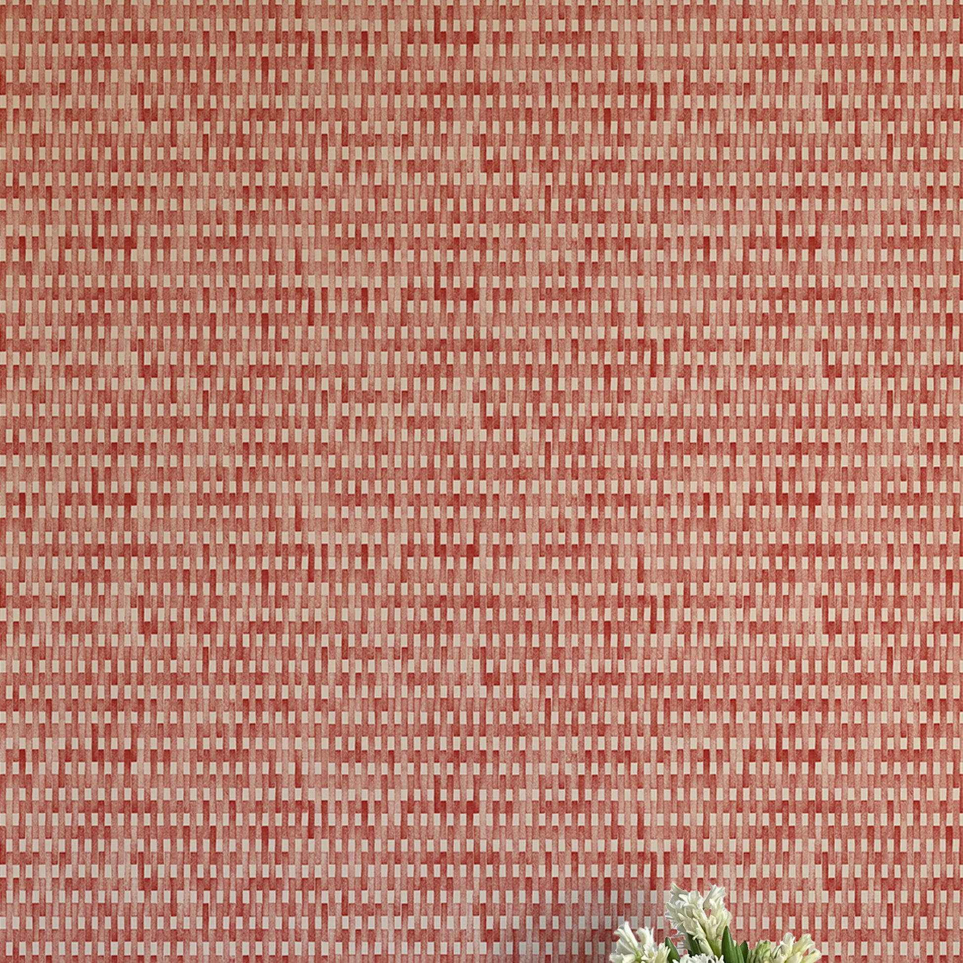 A vase of flowers stands in front of a wall covered in a textural grid print in shades of red and cream.