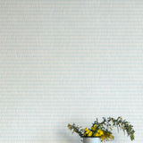 A vase of flowers stands in front of a wall covered in a textural grid print in shades of light blue and cream.