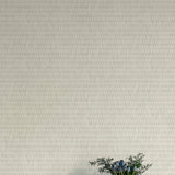 A vase of flowers stands in front of a wall covered in a textural grid print in shades of gray.