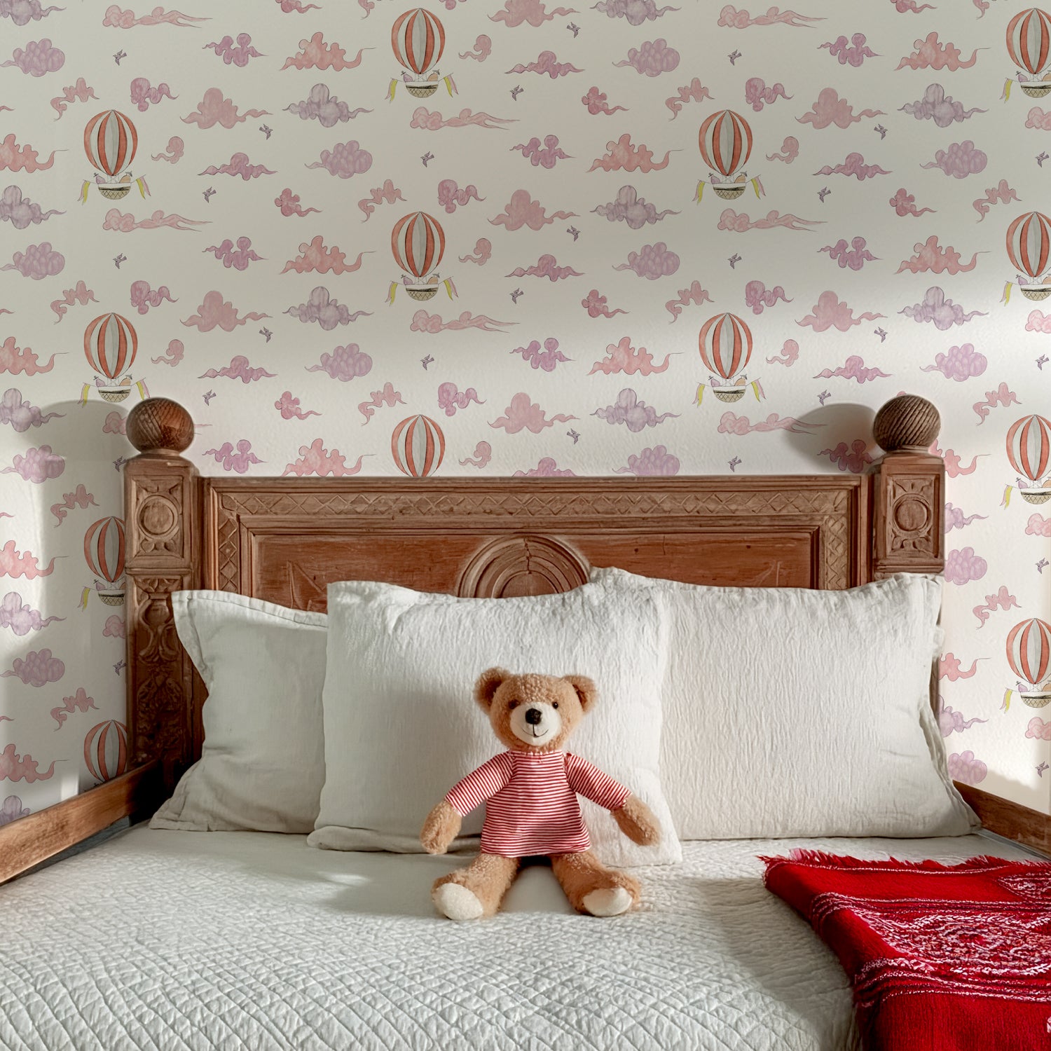 Bedroom with wooden headboard, white pillows, teddy bear, and hot air balloon wallpaper.