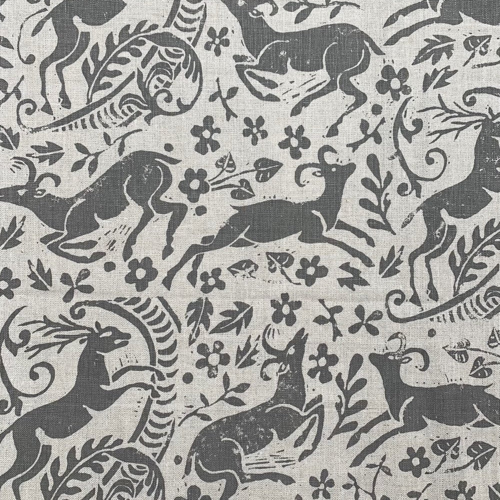 Detail of fabric in a deer, leaf and flower print in gray on a tan field.