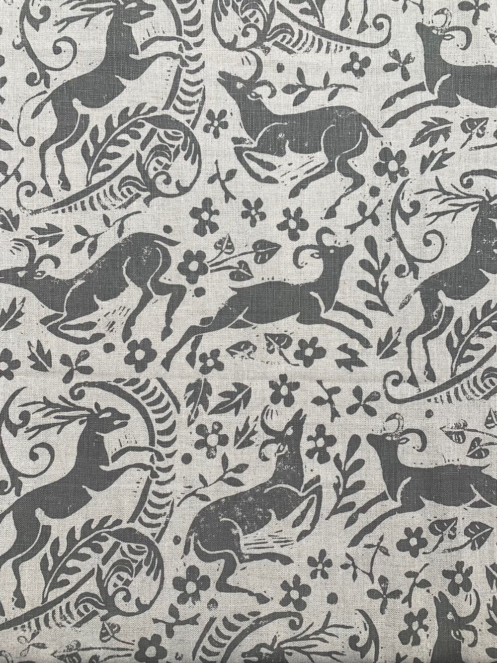 Detail of fabric in a deer, leaf and flower print in gray on a tan field.