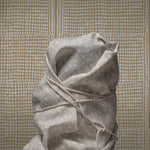 Tied sack made of gray fabric against a patterned wall.