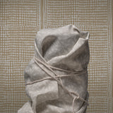 Tied sack made of gray fabric against a patterned wall.