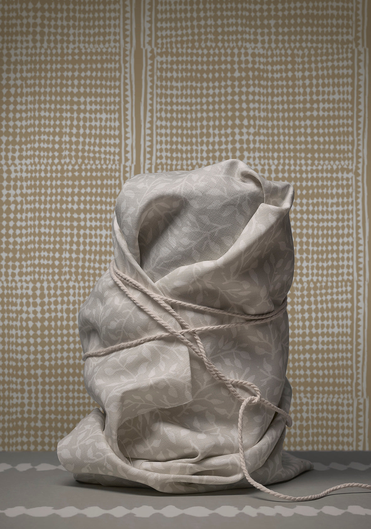 Tied sack made of gray fabric against a patterned wall.