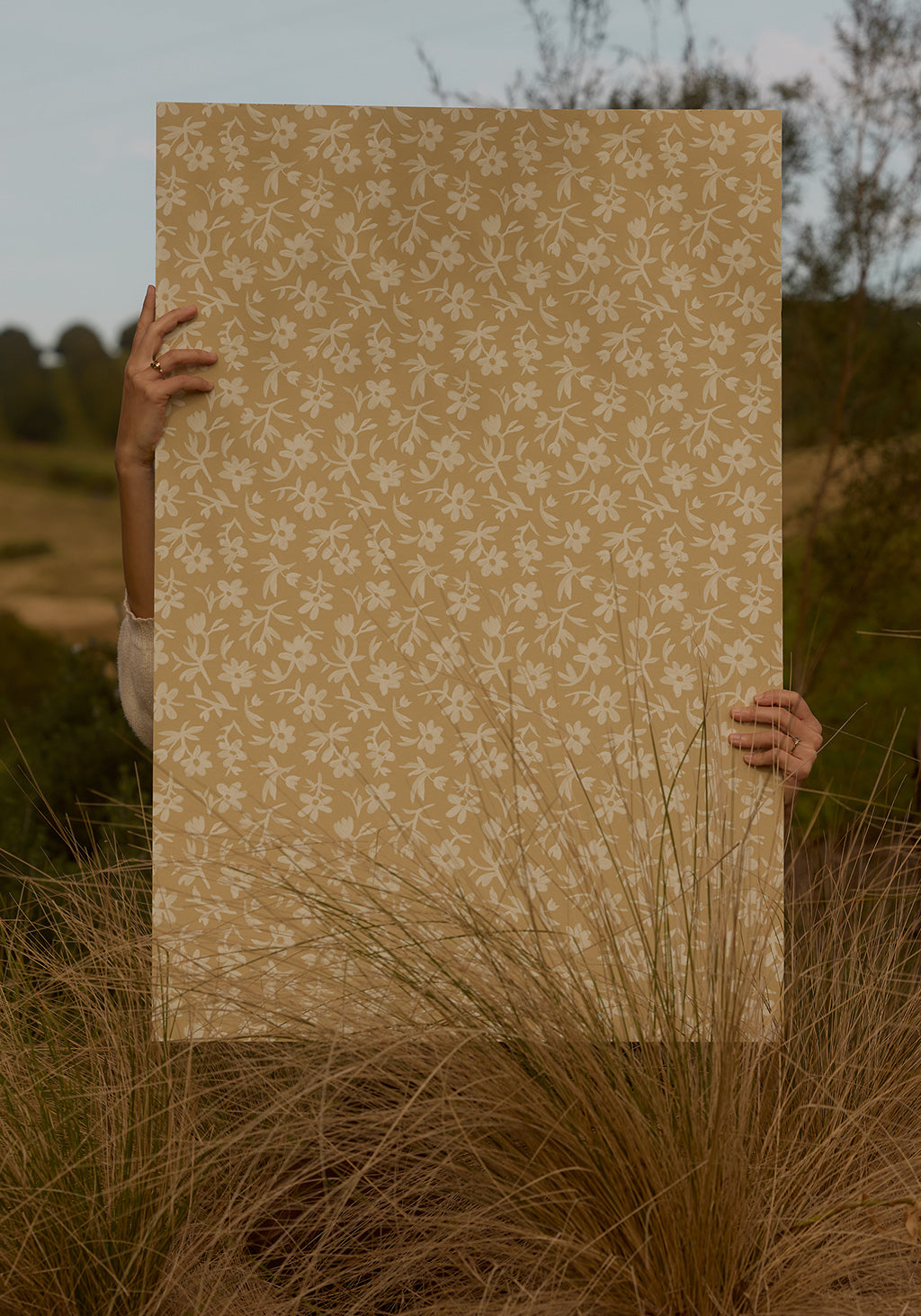 Person holding a large sheet of beige paper with a floral pattern in a natural setting.
