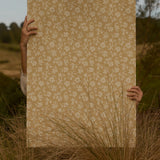 Person holding a large sheet of beige paper with a floral pattern in a natural setting.