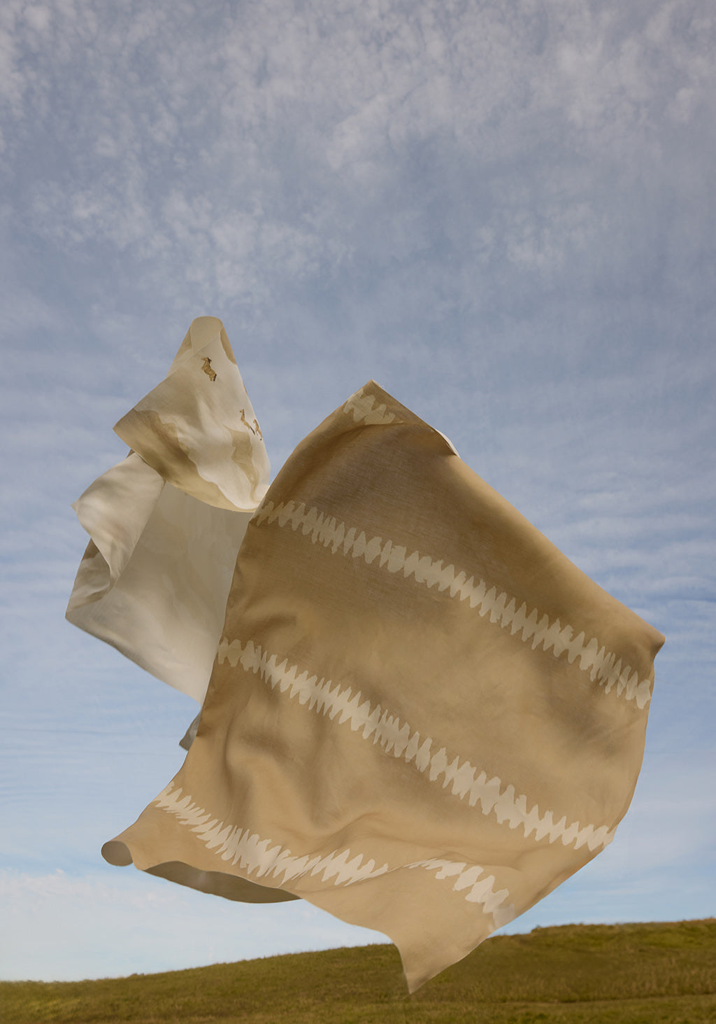 Beige fabric with white patterns blowing in the wind against a blue sky.