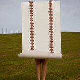 Person holding a brown stripe wallpaper against a grassy field and cloudy sky.