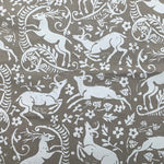 Detail of fabric in a deer, leaf and flower print in white on a light brown field.