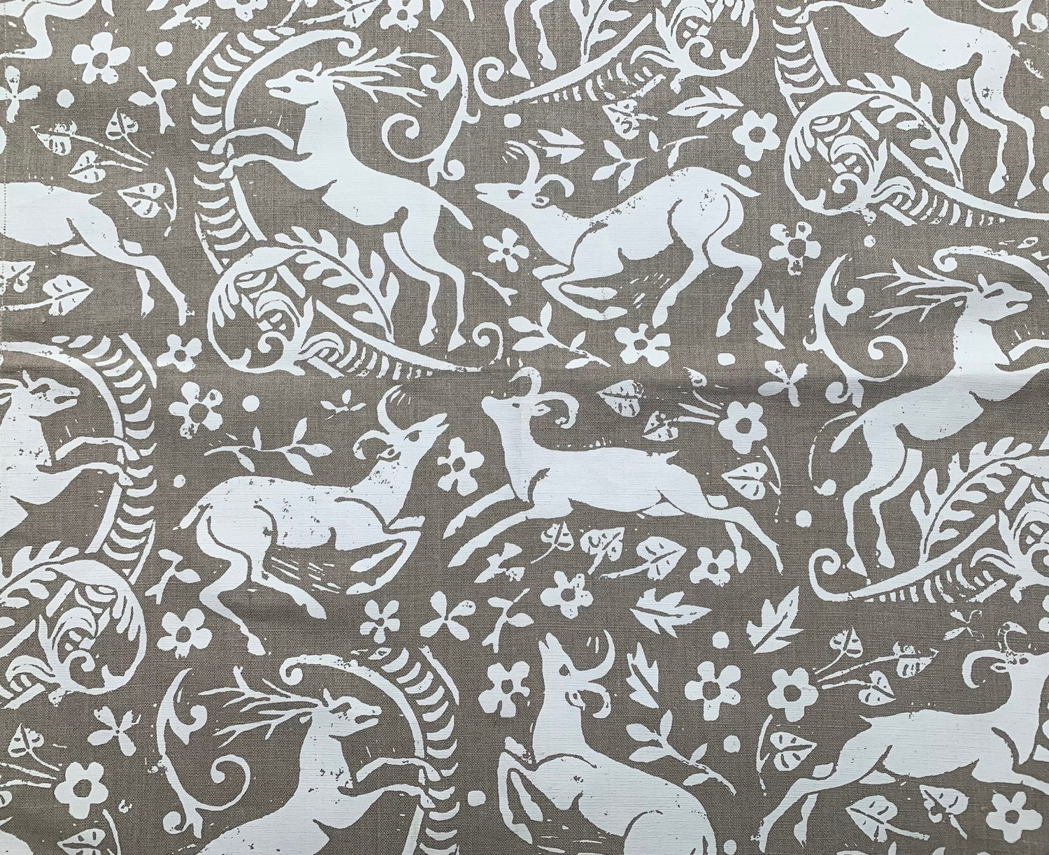 Detail of fabric in a deer, leaf and flower print in white on a light brown field.