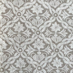 Detail of fabric in a floral lattice print in white on a light brown field.