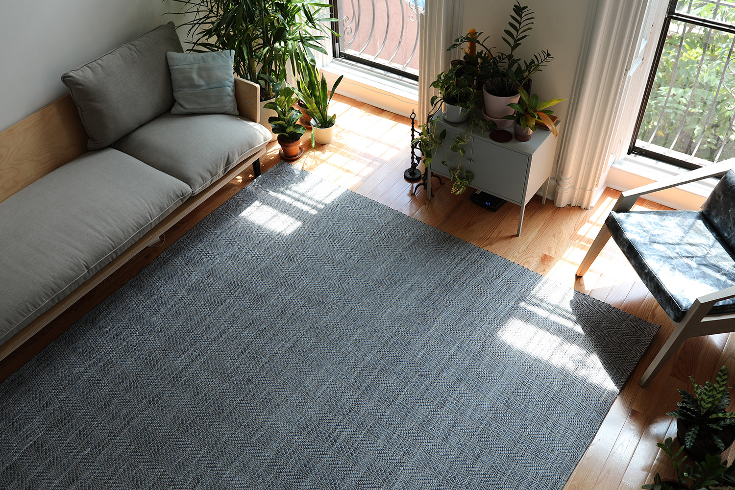 Overhead shot of a plant-filled living room with a woven leather rug in a striped wave texture in shades of gray.