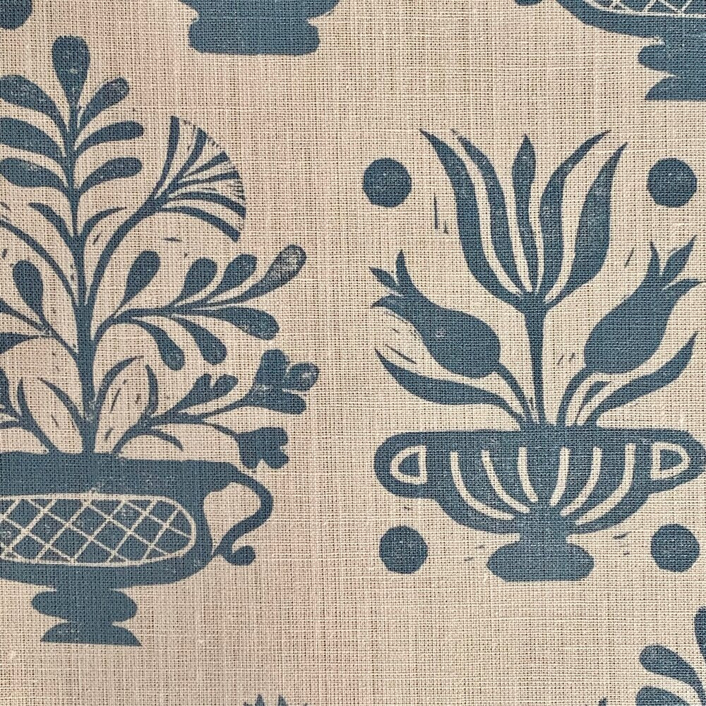 Close-up of fabric in a repeating vase and plant print in blue on a cream field.