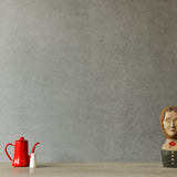 A table with a teapot and bust statue stands in front of a wall papered in mottled gray.