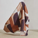 A large piece of draped fabric in a curvilinear geometric print in peach, purple and rust on a white field.