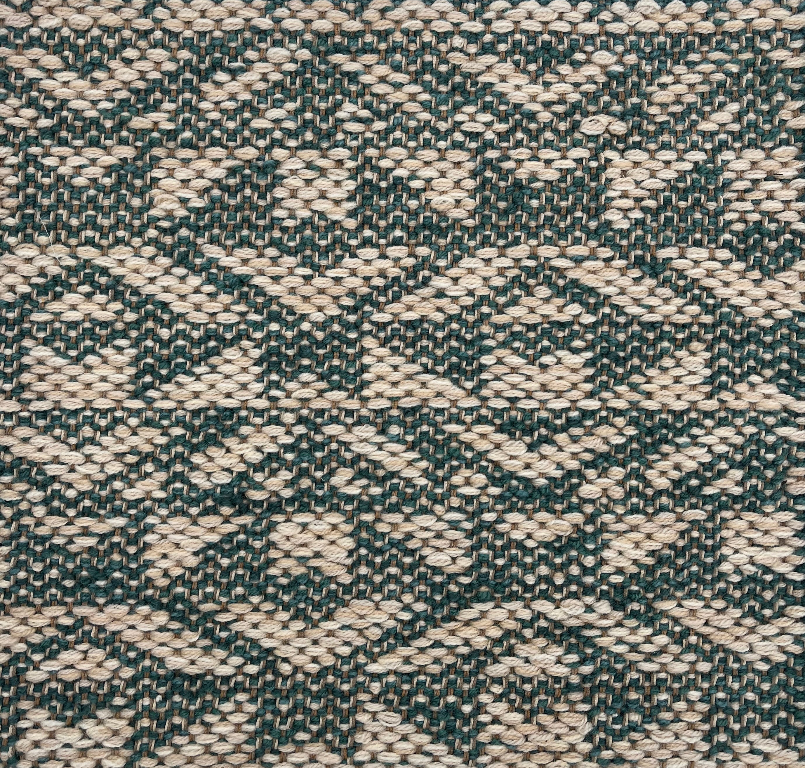 Handwoven rug detail in an angular geometric pattern in teal and beige.