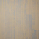 A table with a vase of buds stands in front of a wall papered in mottled gray and blue stripes.