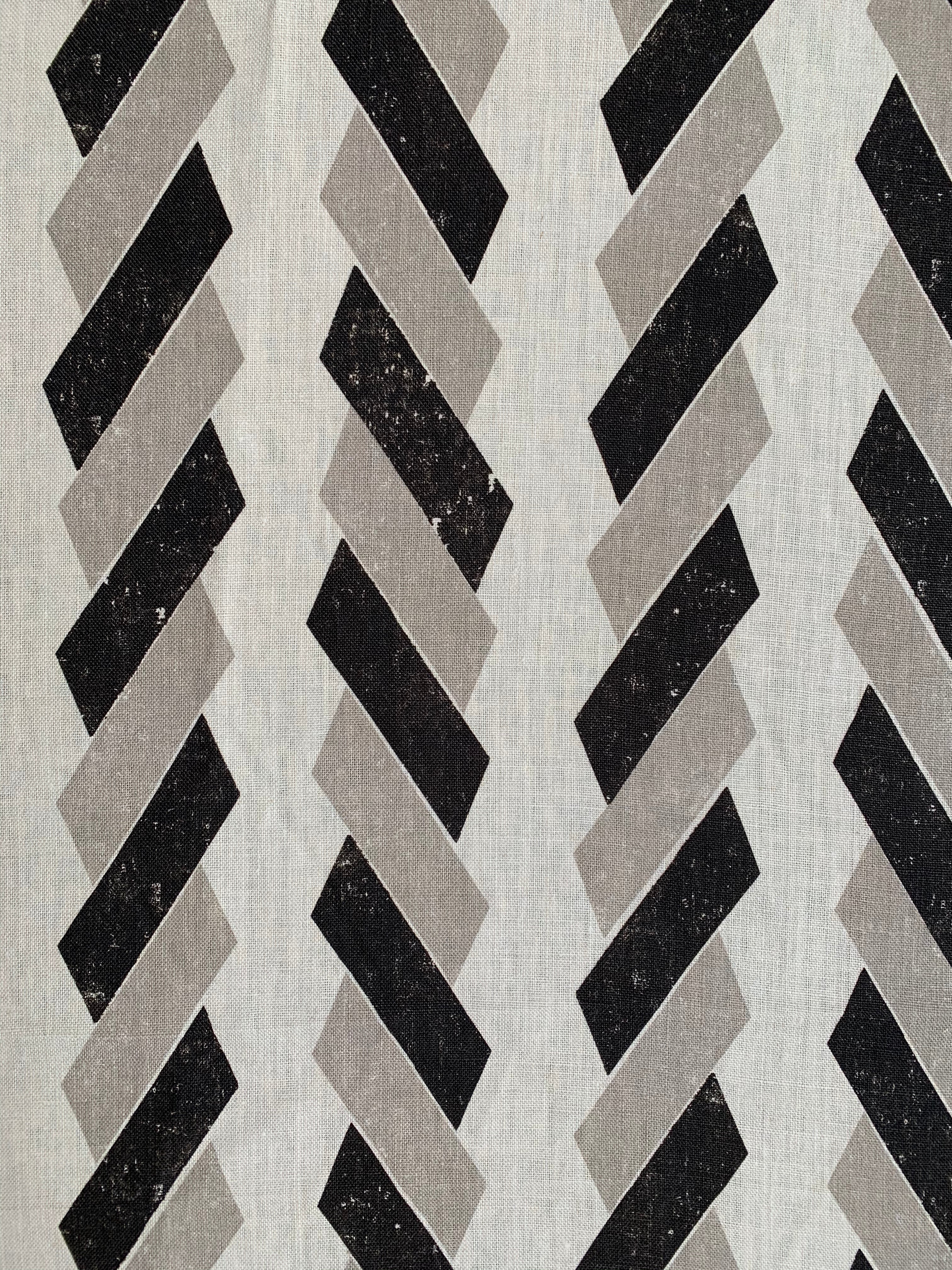 Detail of fabric in a geometric stripe print in black and tan on a white field.