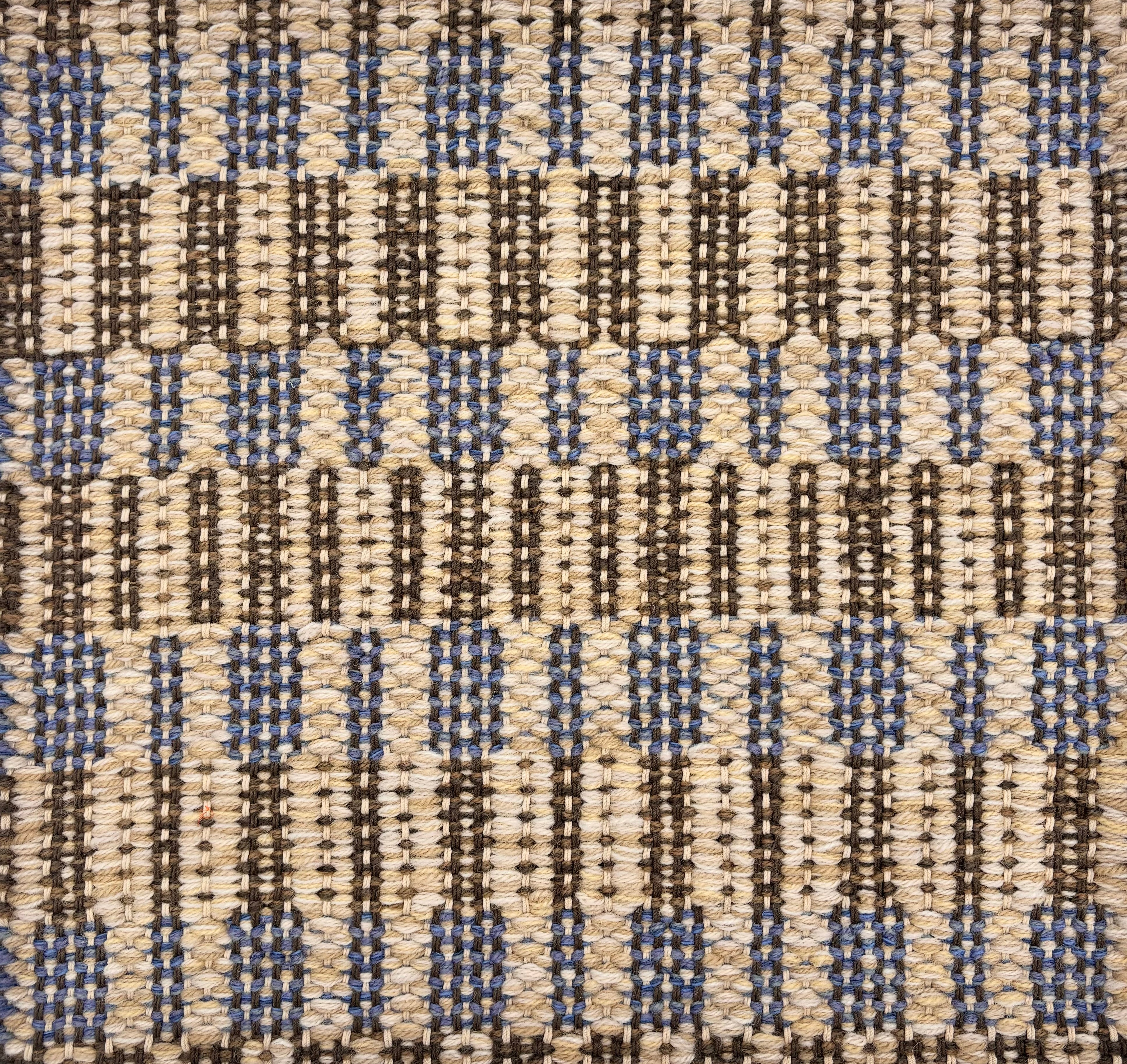 Handwoven rug sample in a stacked blue and brown rectangular stripe design on a cream field. 