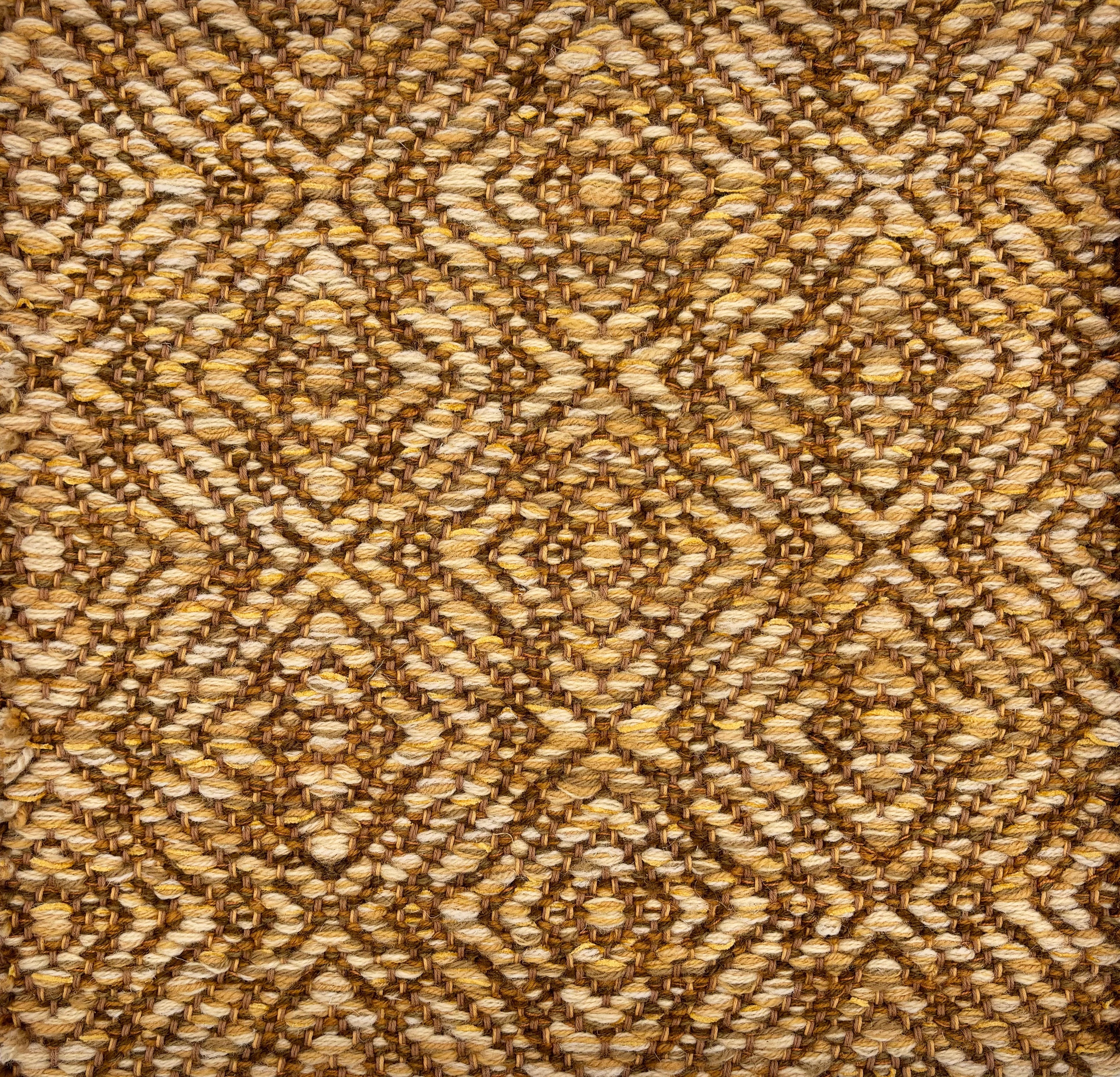 Handwoven rug sample in a radiating diamond pattern in shades of tan and brown. 