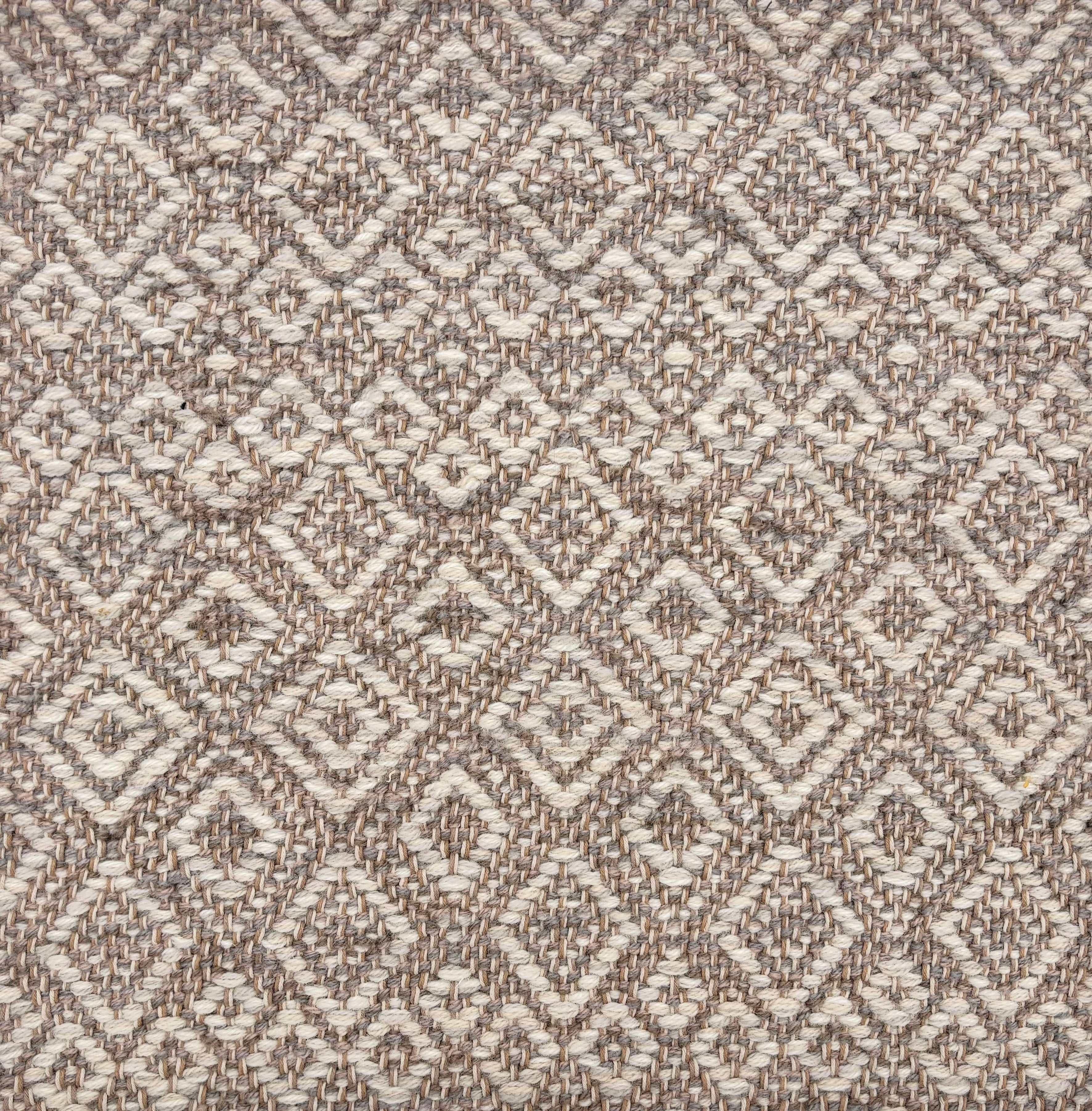 Handwoven rug sample in a radiating diamond pattern in shades of taupe and cream. 