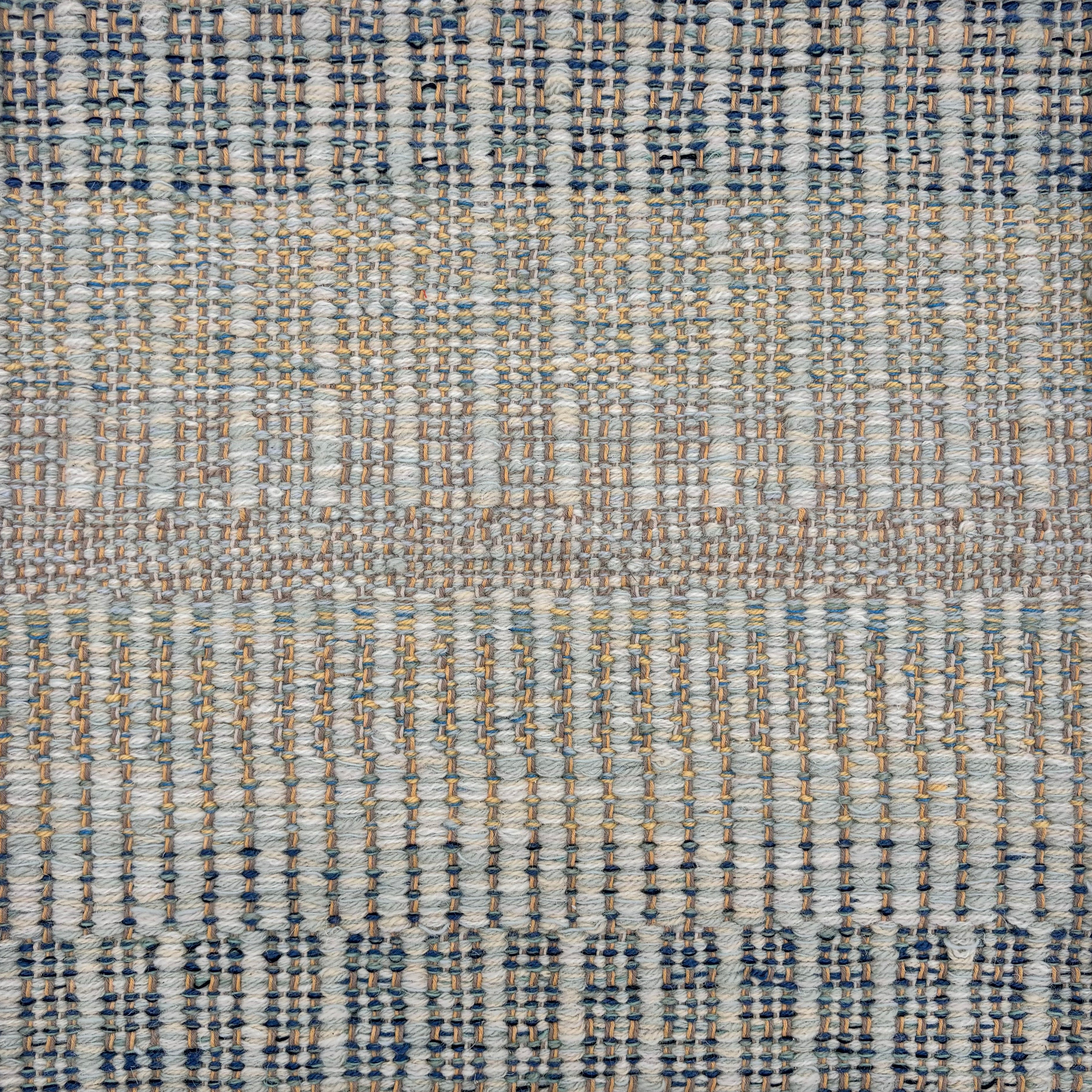 Handwoven rug sample in a textural stripe design in mottled shades blue, grey, tan and yellow. 