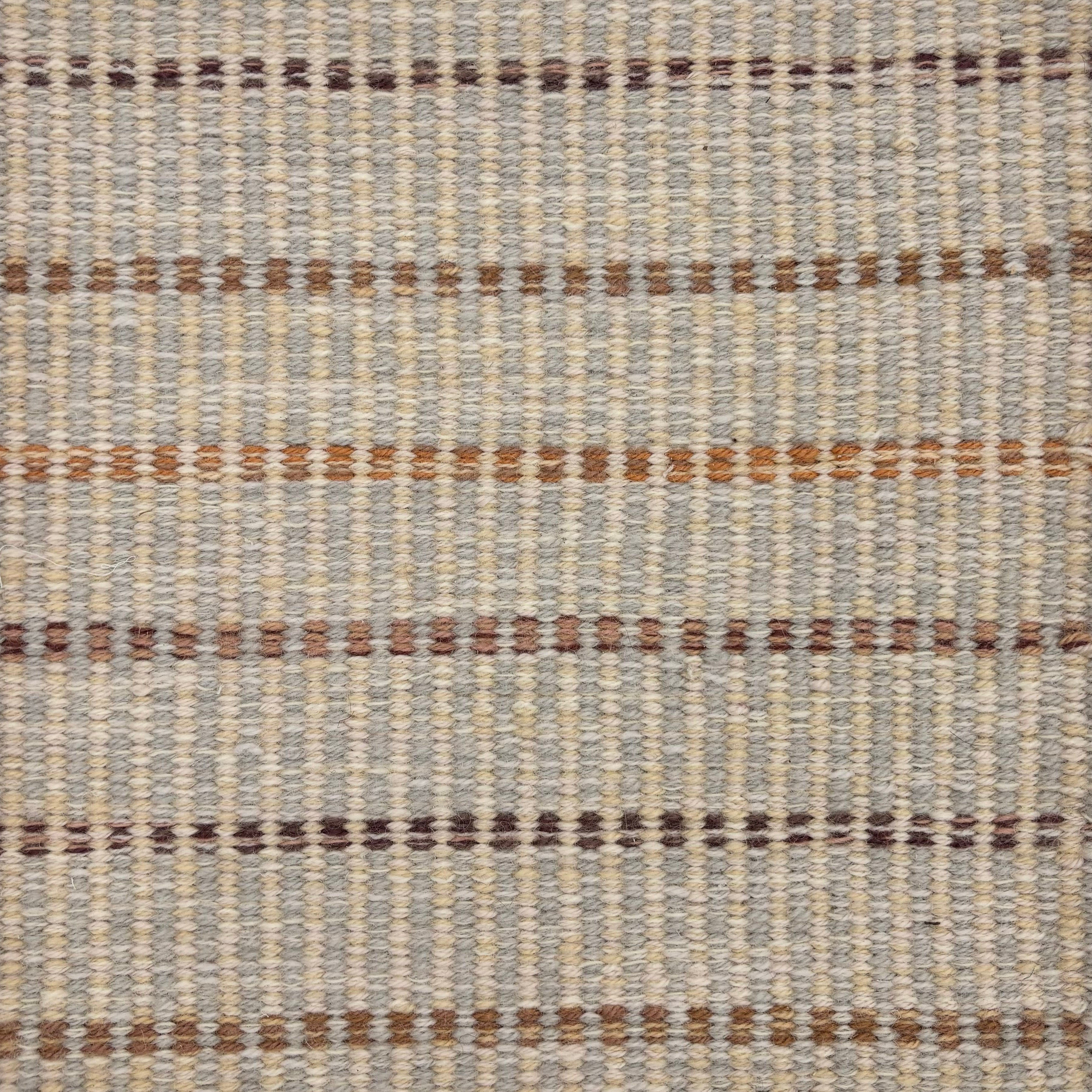 Handwoven rug sample in a striped pattern in shades of brown and tan on a cream and grey field. 