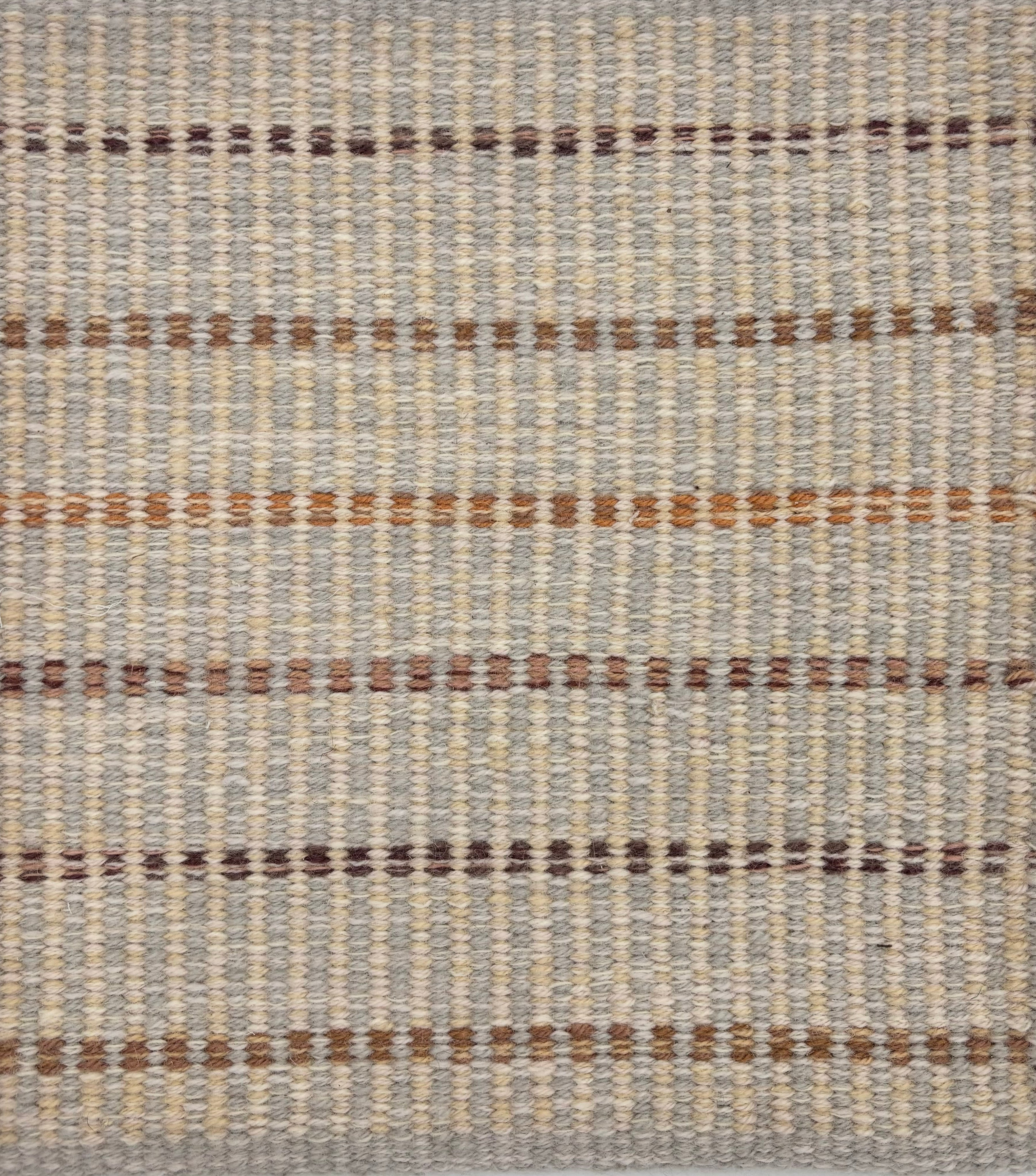 Handwoven rug sample in a striped pattern in shades of brown and tan on a cream and grey field. 