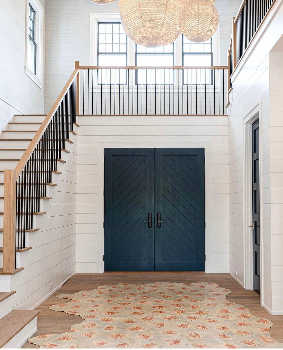 An airy entryway and stairwell space with a cowhide rug in light blue with a painterly flower print in yellow and coral.