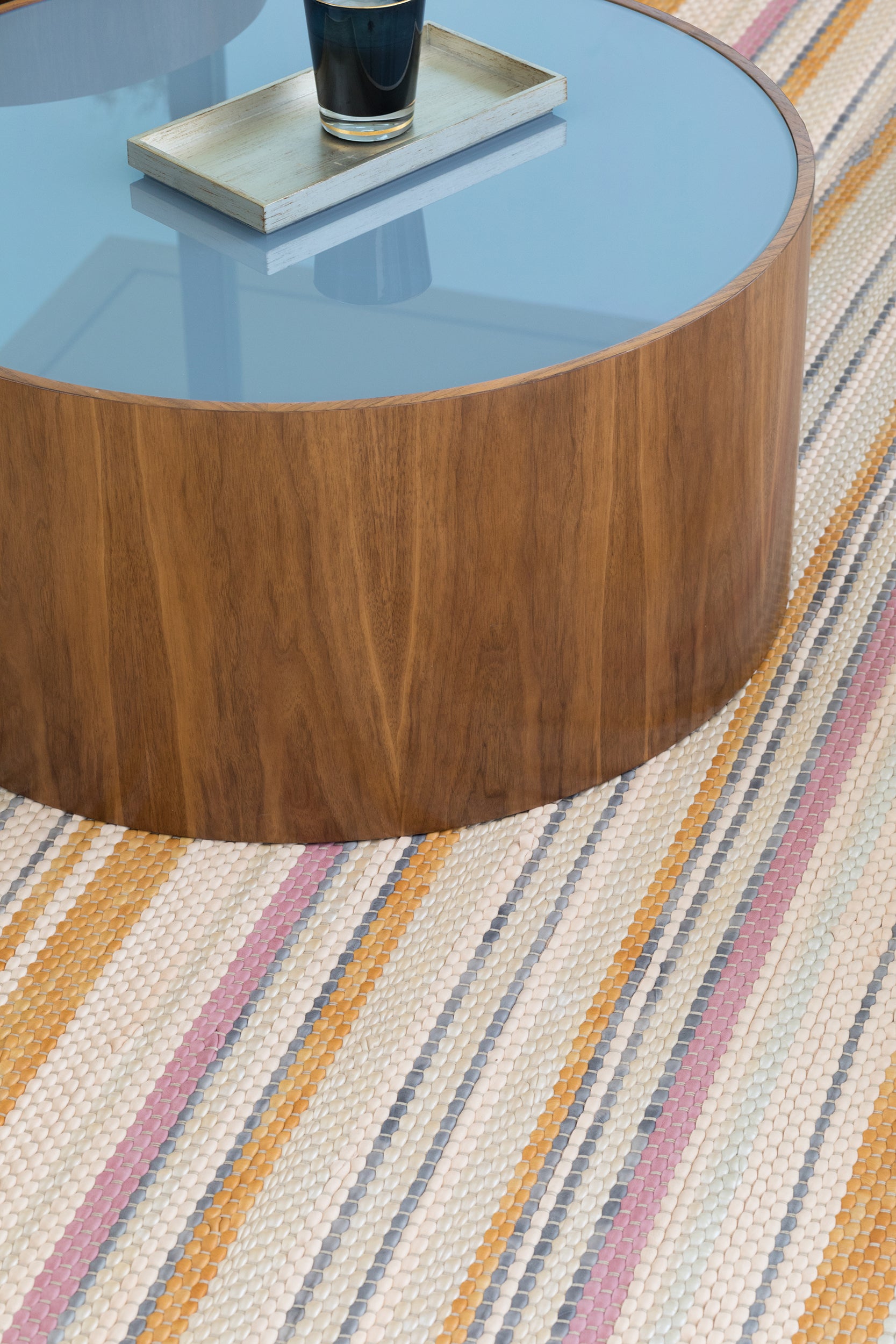 A round coffee table stands on a woven leather rug in an irregular stripe print in shades of pink, yellow and blue.