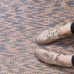 Detail of handwoven leather rug in a graphic geometric pattern in tan and grey with seated woman's legs and oxford shoes. 