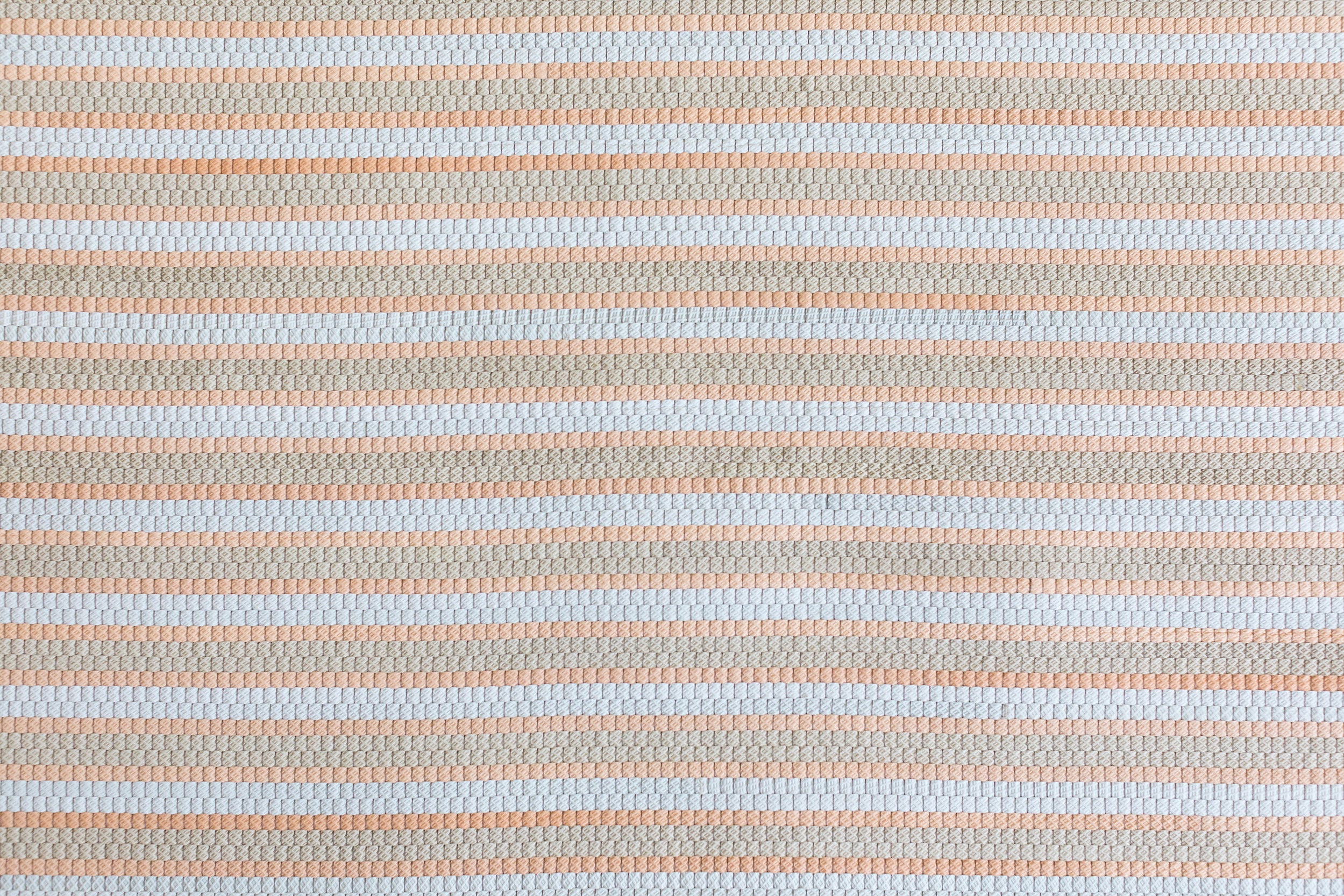 Detail of a woven upholstery leather in a striped coral, tan and white colorway.