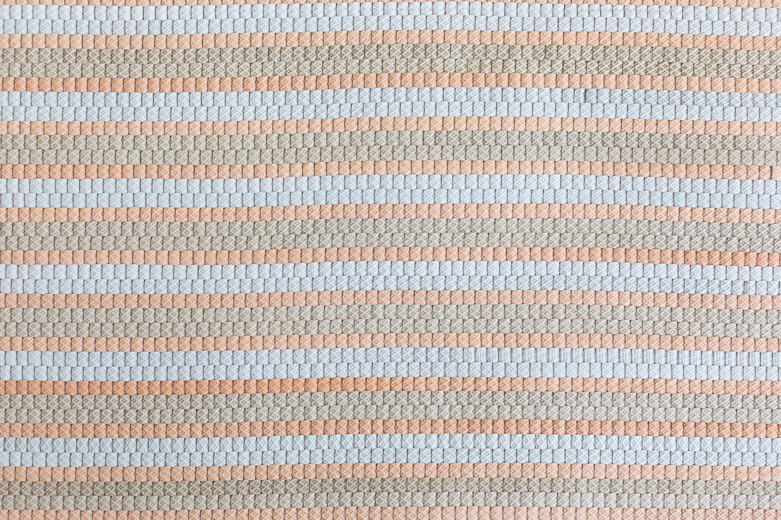 Detail of a woven upholstery leather in a striped coral, tan and white colorway.