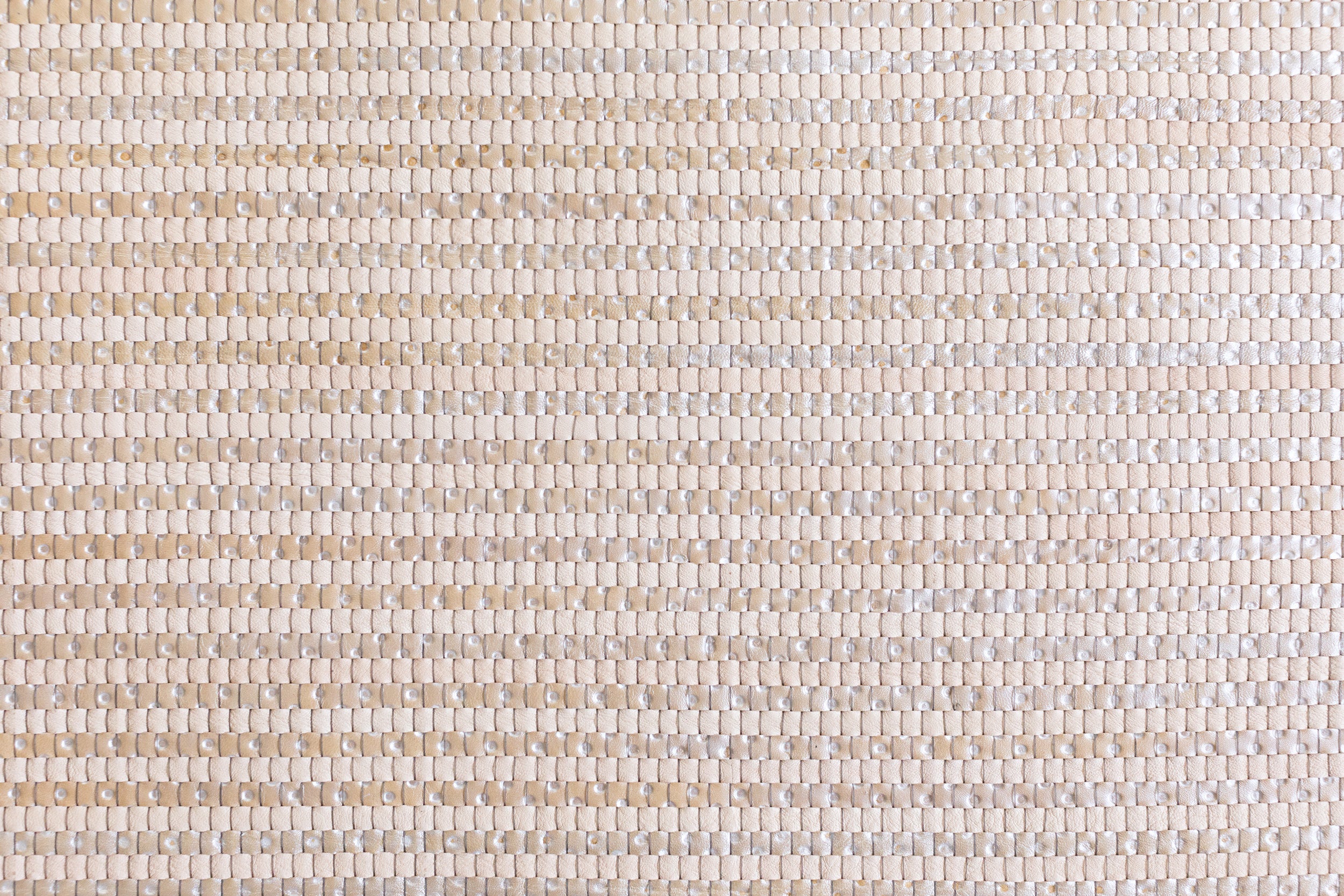 Detail of woven upholstery leather in a grid pattern in metallic tan.