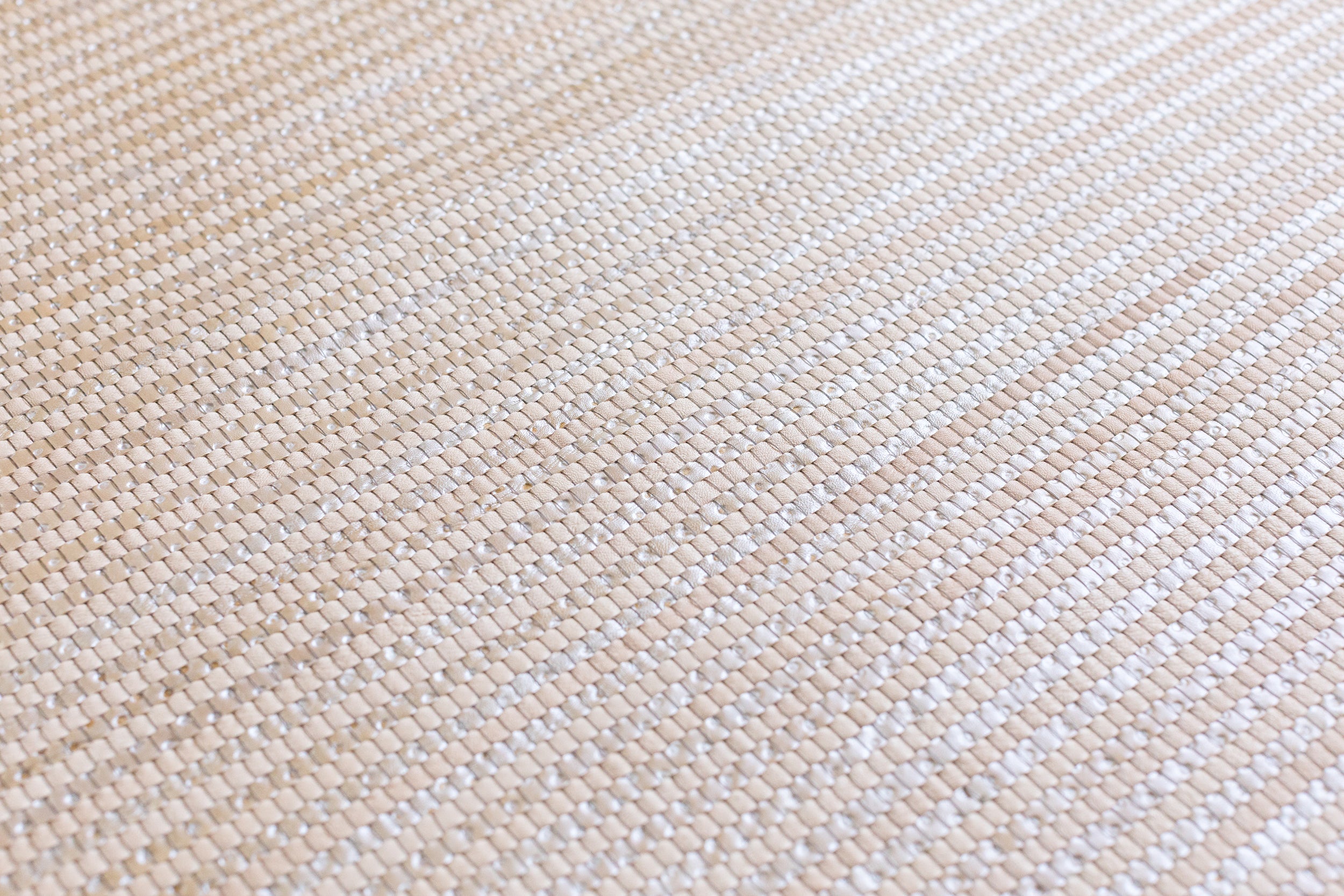 Detail of woven upholstery leather in a grid pattern in metallic tan.