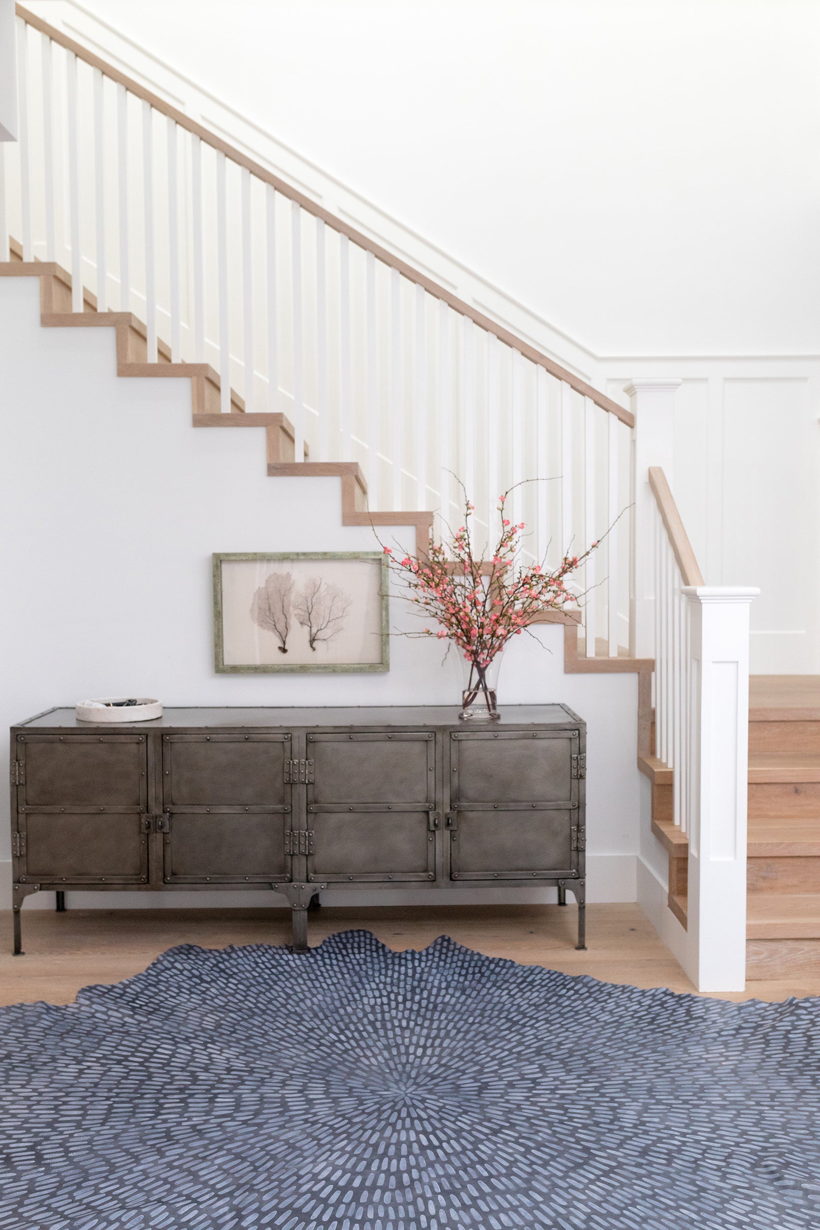 A sunny stairwell with a large cowhide rug in navy with a painterly starburst overlay in blue.