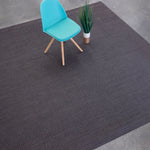 Overhead shot of a chair sitting on a woven leather rug in a herringbone pattern in mottled gray with pink accents.