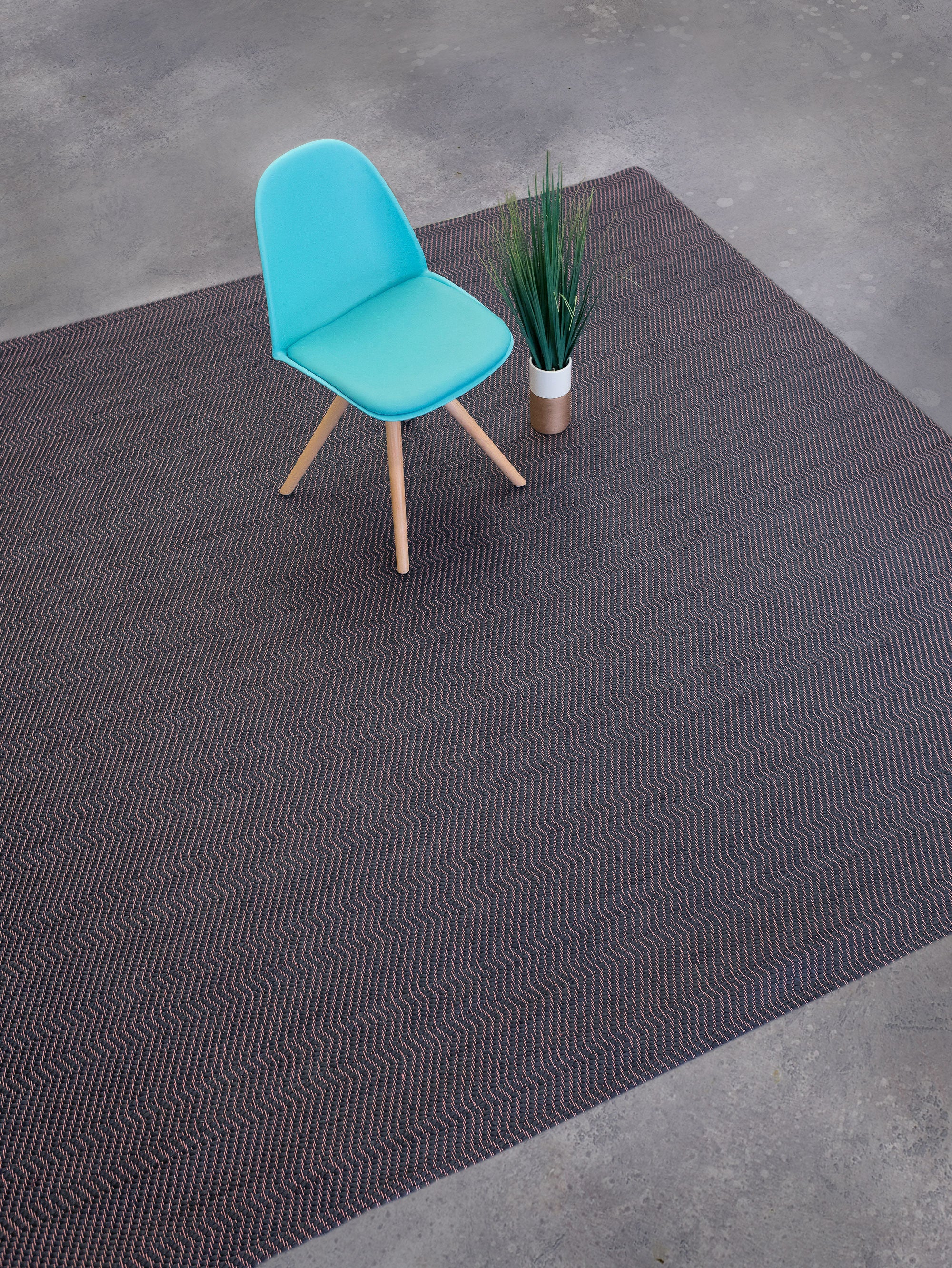 Overhead shot of a chair sitting on a woven leather rug in a herringbone pattern in mottled gray with pink accents.