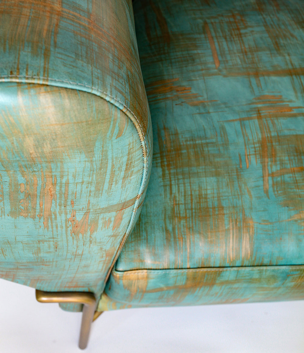 Close-up of a modernist armchair upholstered in leather in a textural brushstroke pattern in turquoise and gold.